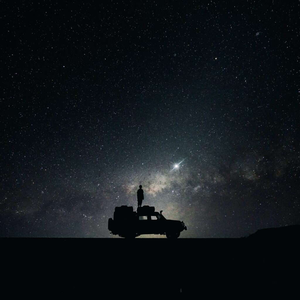 man standing on jeep with starry sky